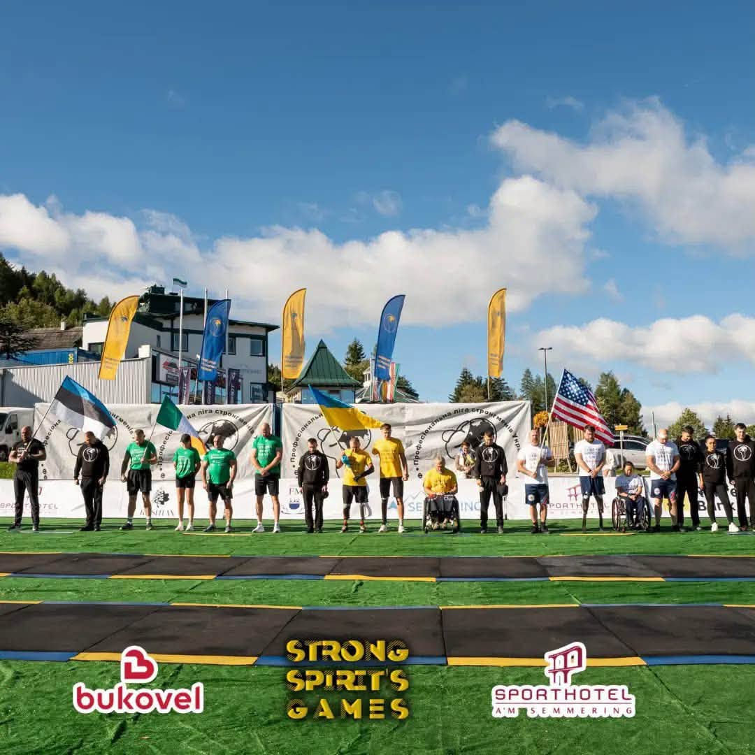 Учасники змагань Strong Spirit's Games у жовтих та синіх спортивних костюмах стоять на лінії фінішу на фоні прапорів США та