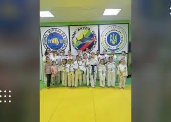 Юні спортсмени в білих кімоно та жовтих поясах позують на жовтому татамі перед логотипами федерацій таеквон-до