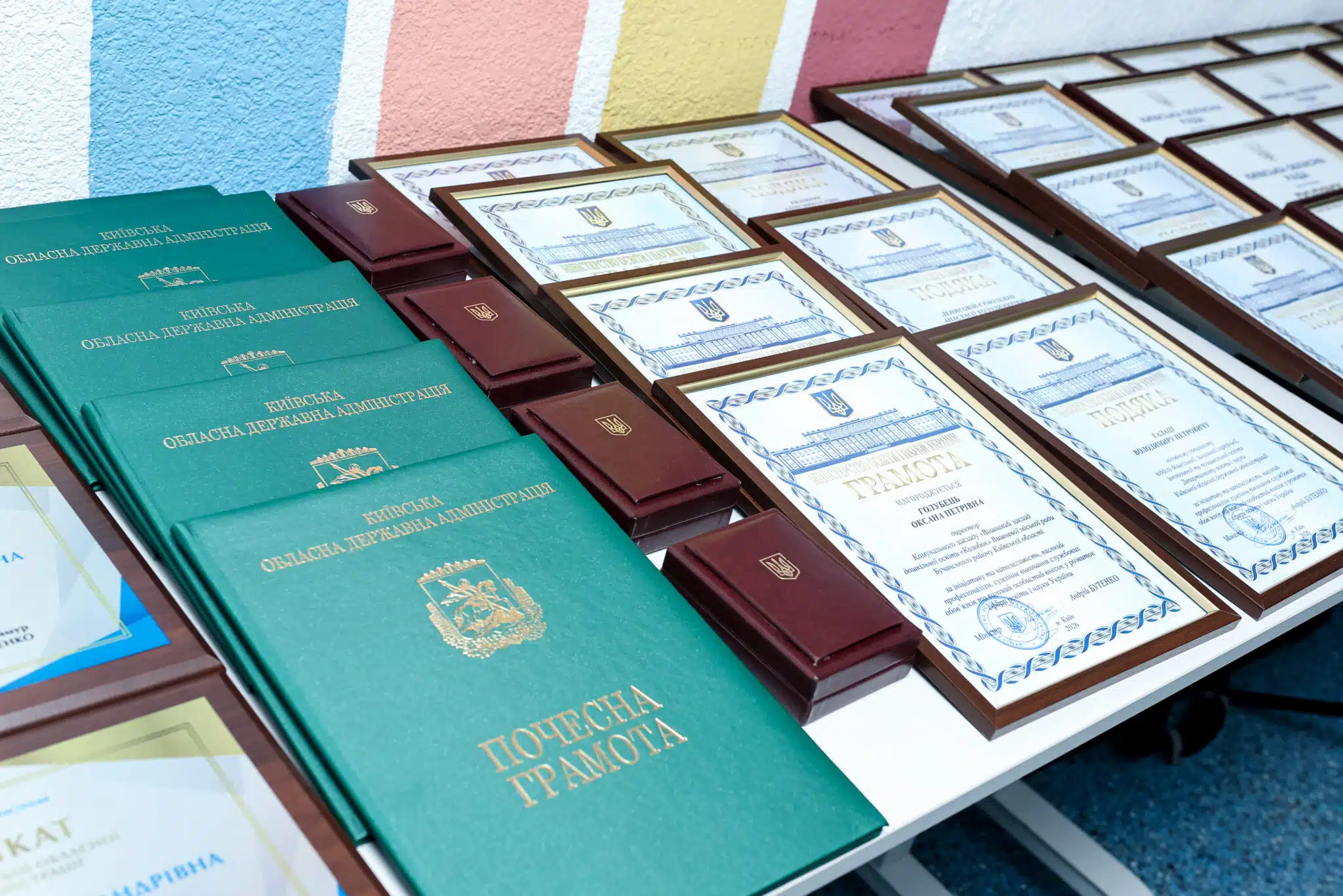 Зелені та бордові папки з грамотами та свідоцтвами на столі під кольоровим фоном стіни