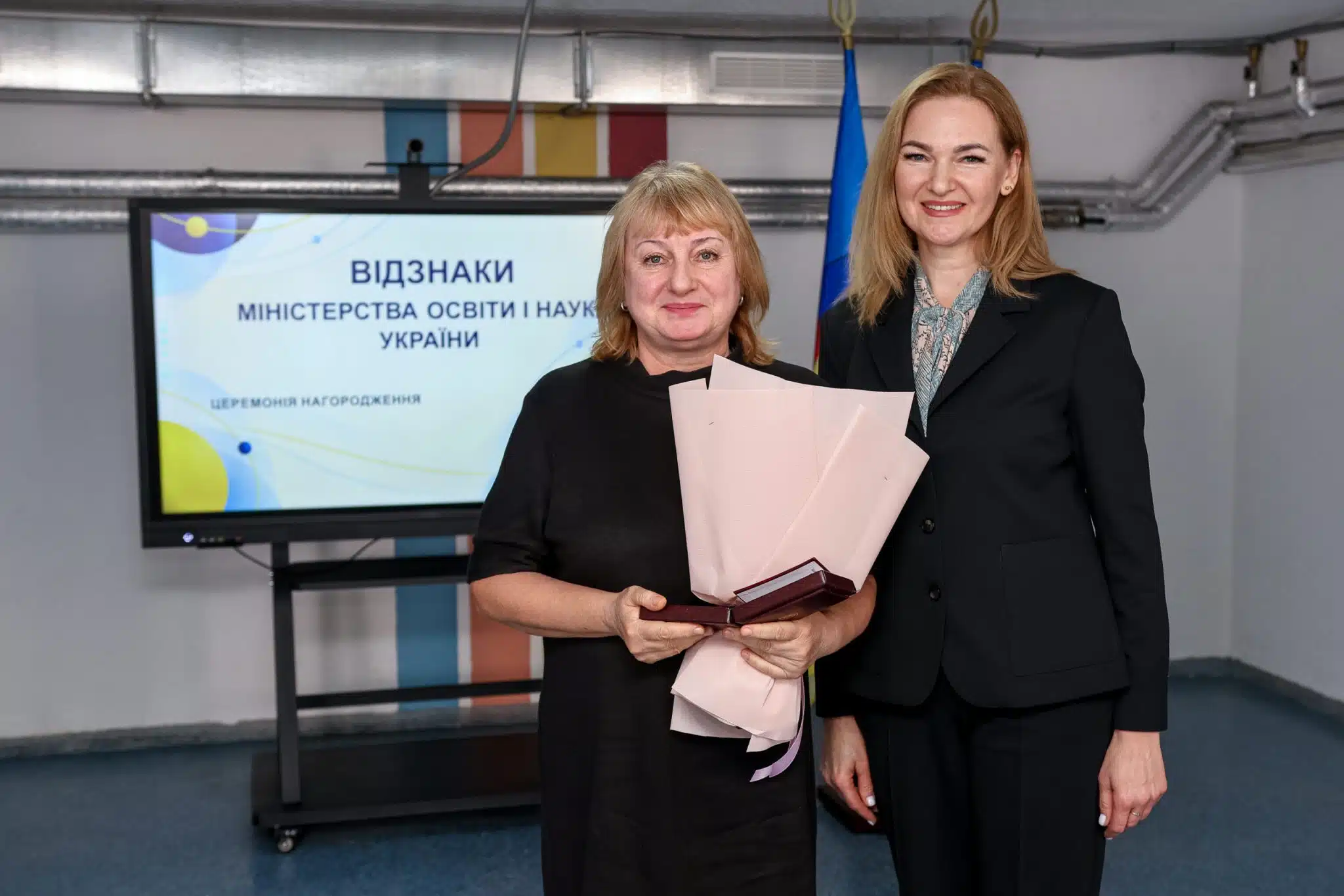 Дві жінки позують для фото з сертифікатом перед екраном та прапором Філіппін