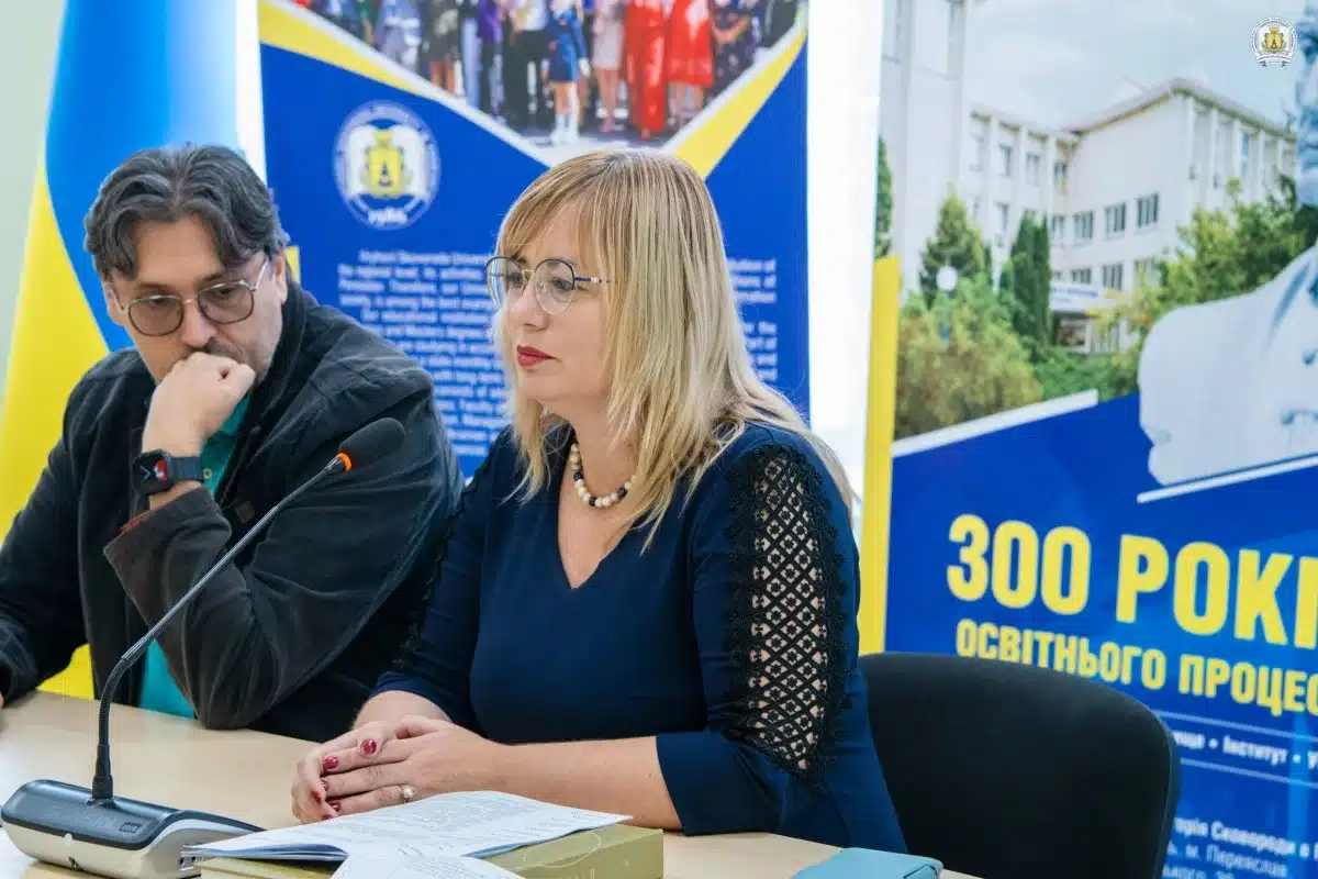 Чоловік та жінка сидять за столом із мікрофонами під час пленарного засідання конференції