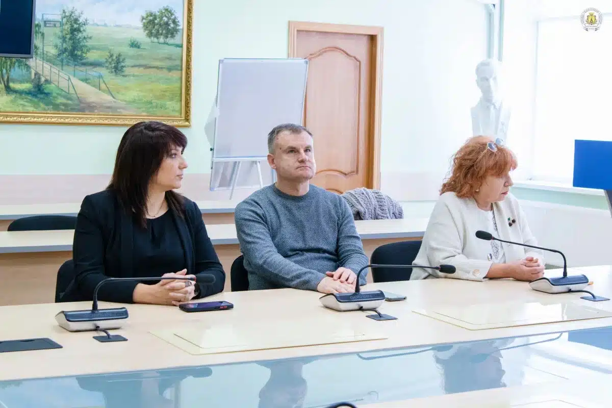 Три людини сидять за столом із мікрофонами під час презентації у конференц-залі