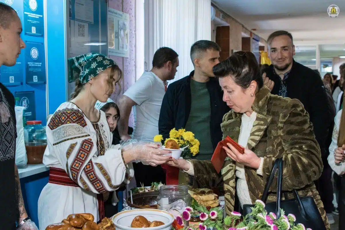 Дівчина в українському вишиванці дарує квіти жінці в золотистому піджаку на благодійному ярмарку
