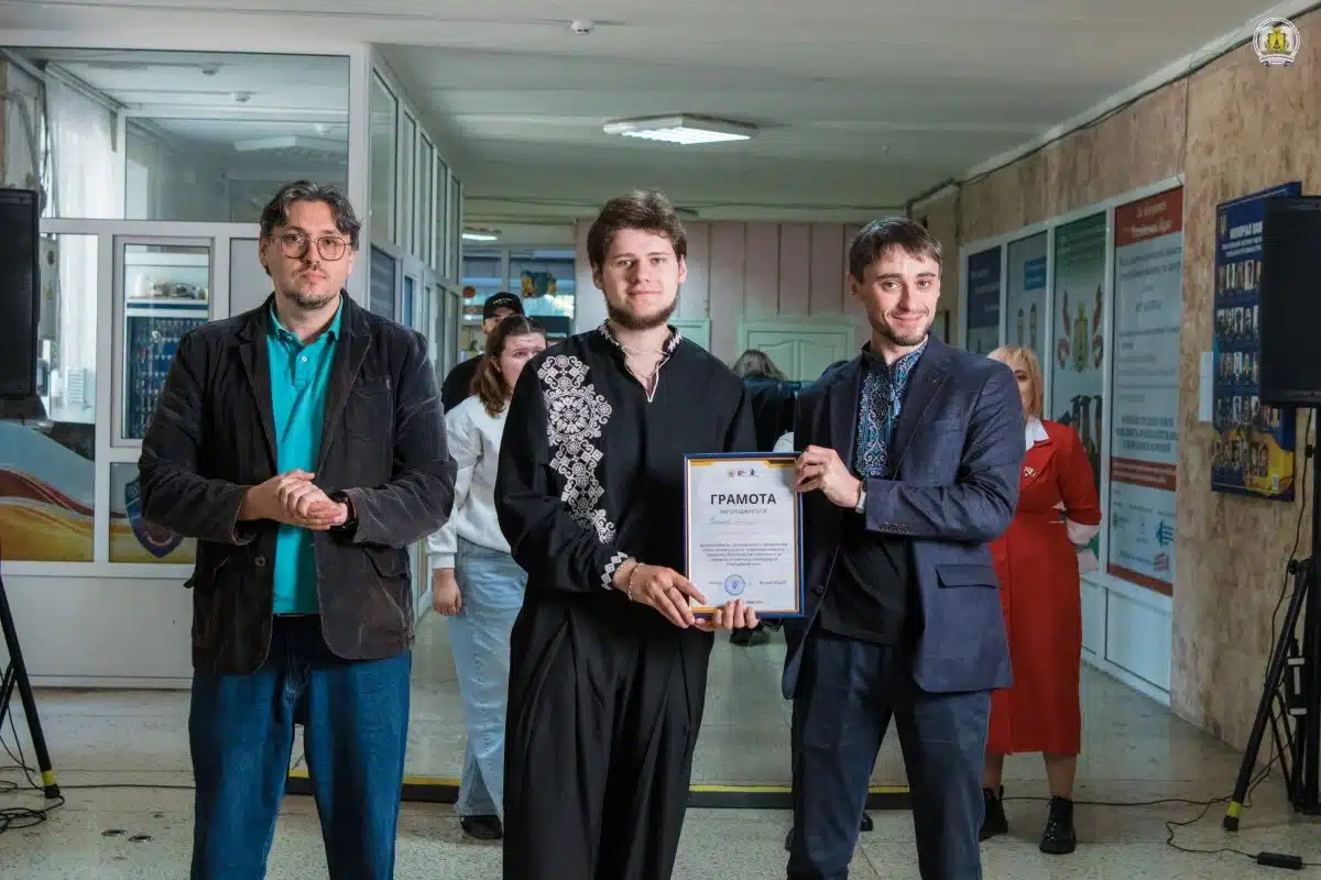 Троє чоловіків у піджаках тримають грамоту, отриману під час проведення ярмарку в університеті