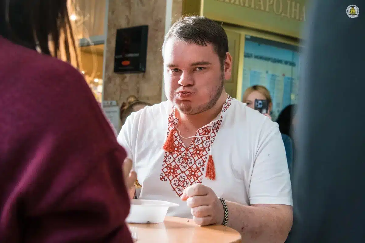 Молодий чоловік у білій сорочці з вишивкою розмовляє з жінкою в коридорі закладу під час заходу