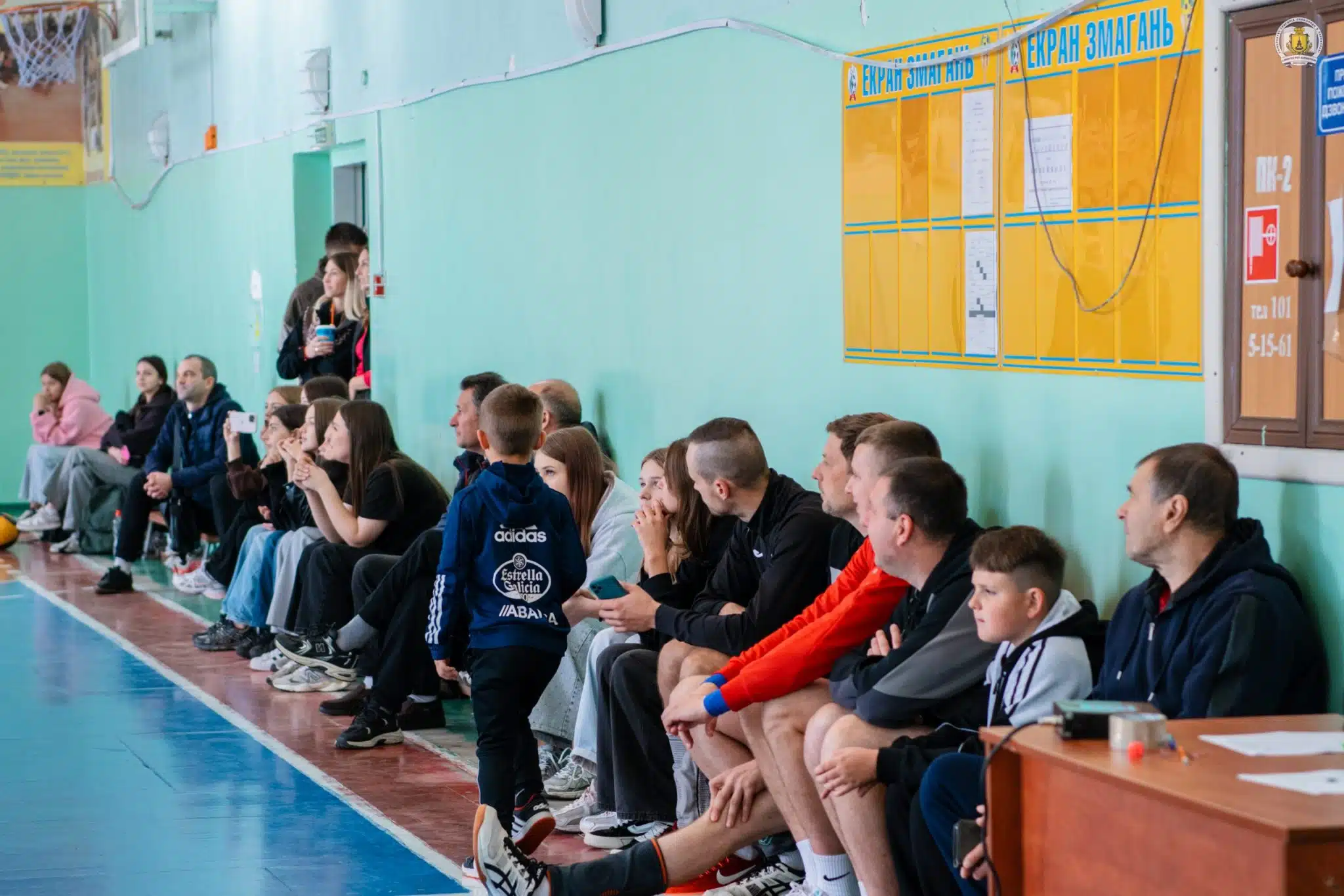 Глядачі та учасники команд сидять у залі і спостерігають за волейбольним матчем