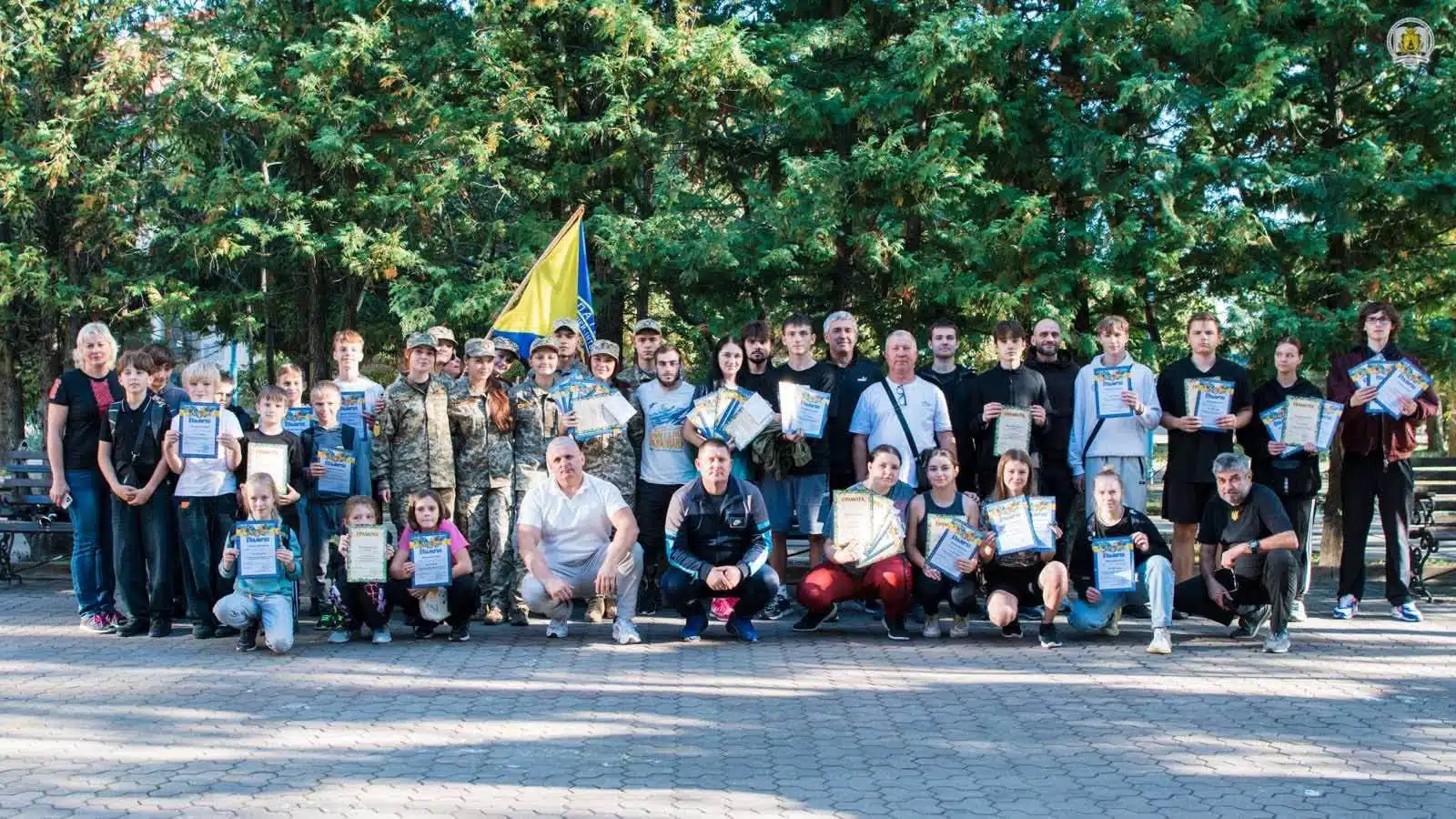 Велика група учасників змагань з сертифікатами збирається на церемонію нагородження з українським прапором