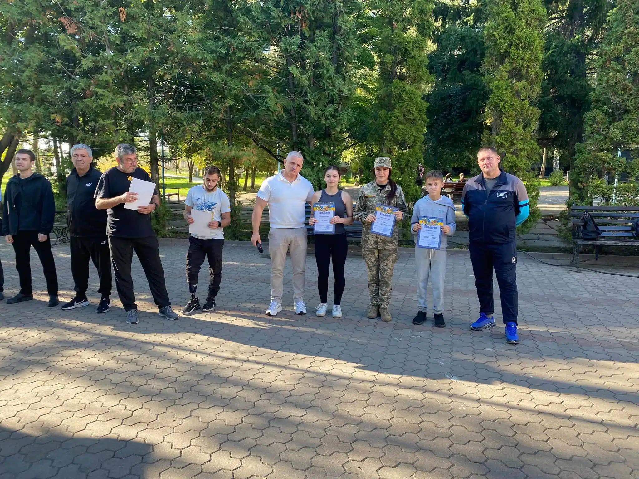 Учасники змагань зі сертифікатами стоять у ряд на церемонії нагородження в парку